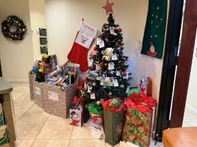 Christmas tree surrounded by wrapped gift bags, toy donation boxes, and festive decorations in a dental office.