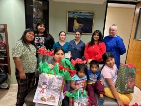 Families and dental staff gathered with holiday gift bags, surrounded by children holding presents.