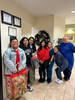 Group photo of dental staff and community members holding holiday gift bags near a festive wreath.