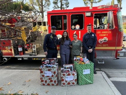 Firefighters and dental staff posing with toy donation boxes in front of a Los Angeles County fire truck.